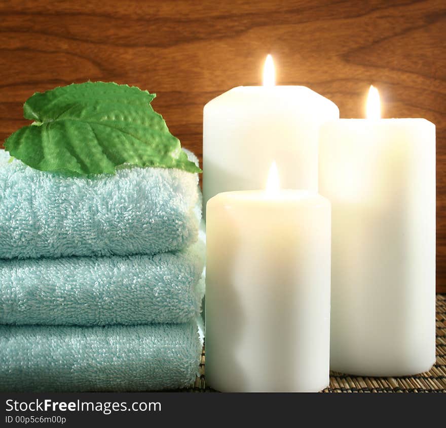 Blue towel, white candle, green leaf in front of wood background. Blue towel, white candle, green leaf in front of wood background