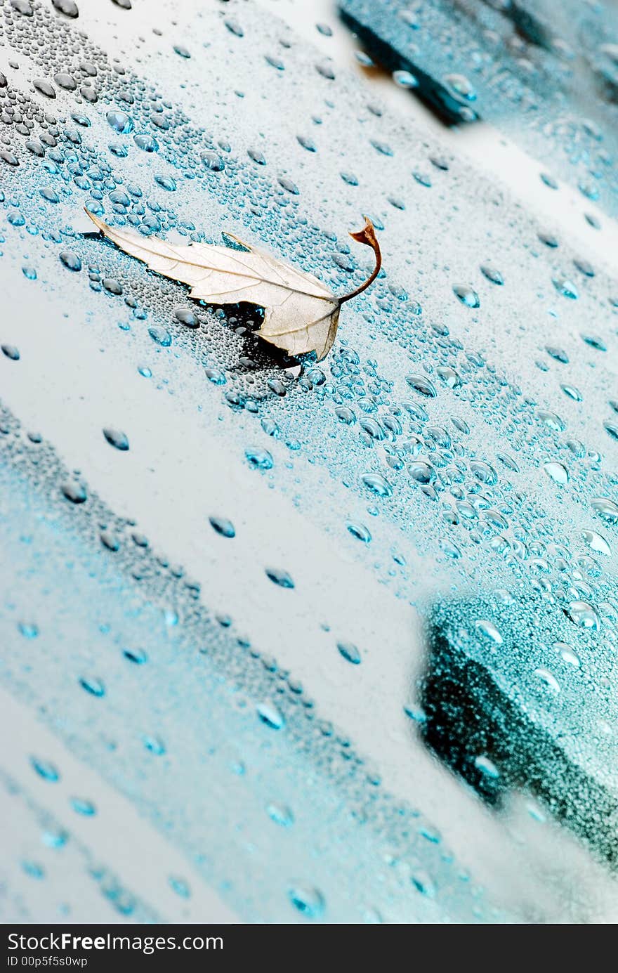 Droplets and a leaf on a blue glass.The top righ corner and the bottom left corner are out of focus