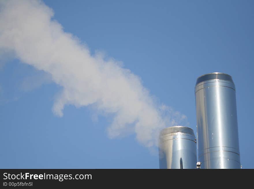 Two chimneys with a smoke on a background of the blue sky