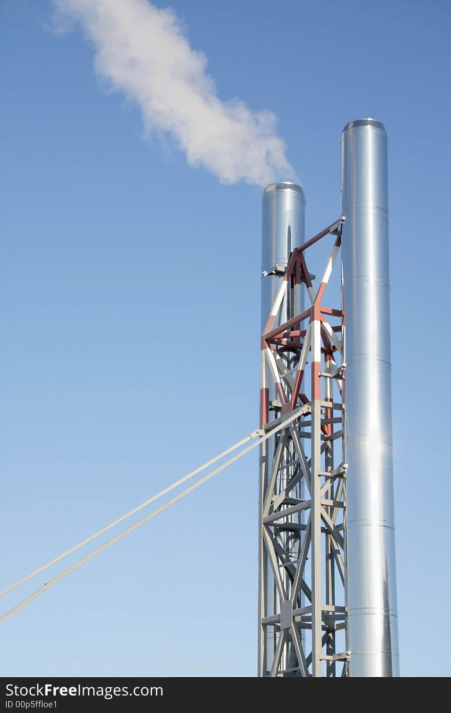 Two chimneys on a metal farm with a smoke on a background of the blue sky