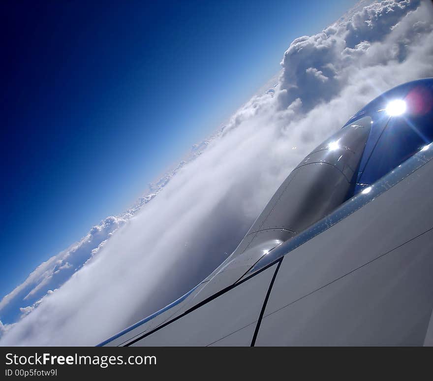 Photo of an airplane engine taken from inside the plane while flying above blue skies and fluffy white clouds. Photo of an airplane engine taken from inside the plane while flying above blue skies and fluffy white clouds.