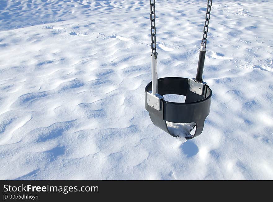 A lonely swing over the snow in a playground.