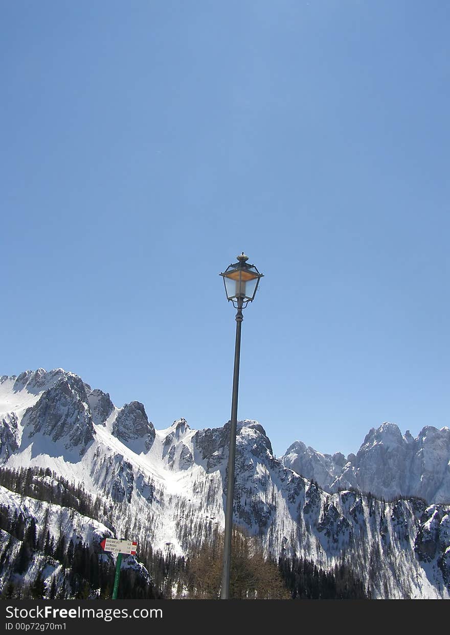 Vintage lamp in mountain village, beautiful mountain peaks and alpine vegetation covered in snow, clear blue sky winter day