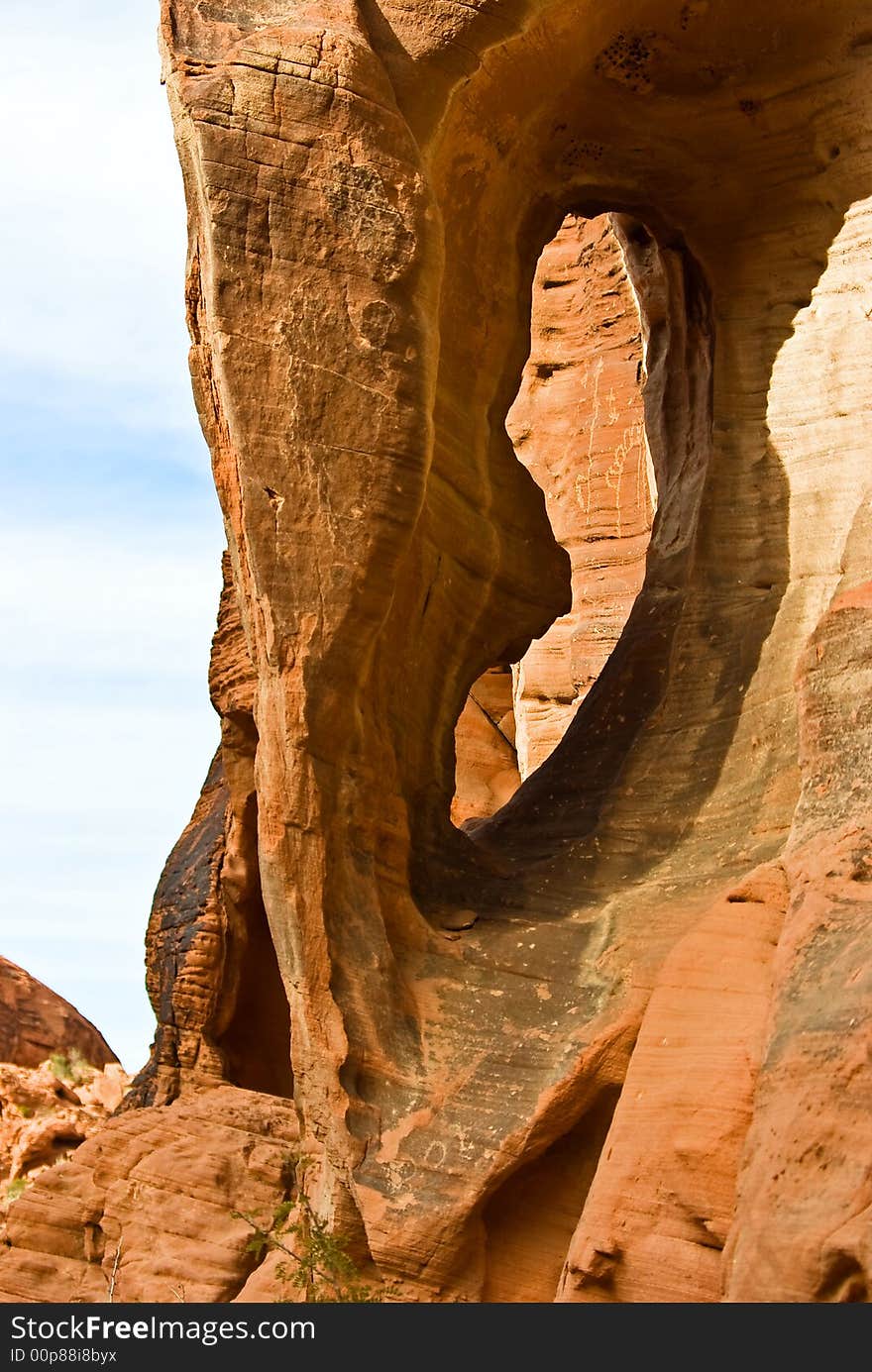 Rock formation with arch and Native American petroglyphs on canyon wall in background - Valley of fire SP