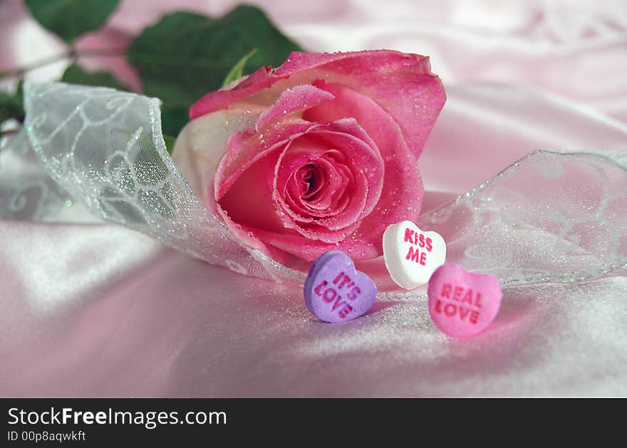 Single pink rose with sparkling ribbon and candy hearts on satin. Single pink rose with sparkling ribbon and candy hearts on satin.