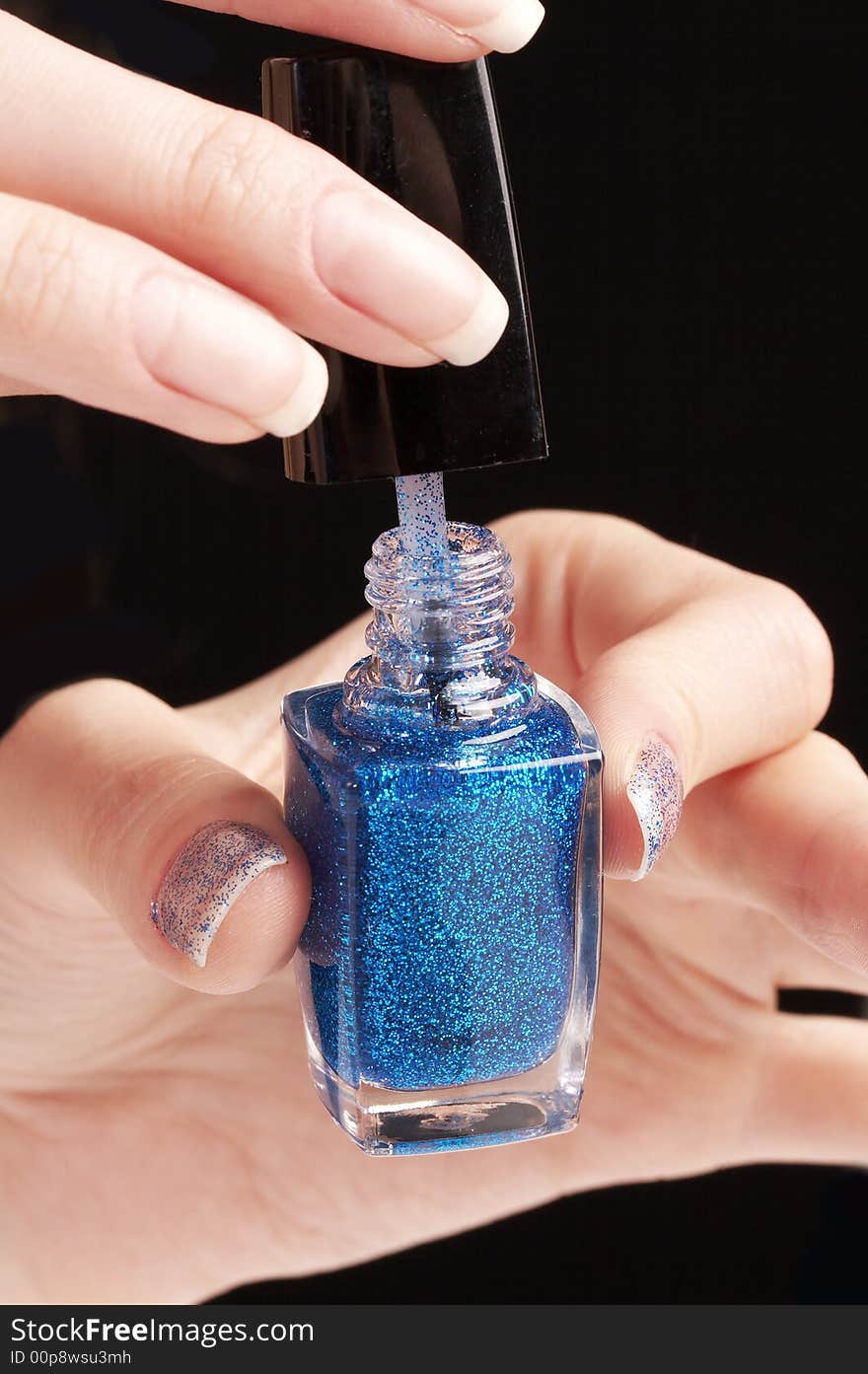 Woman applying blue glittering nailpolish, party manicure , black background