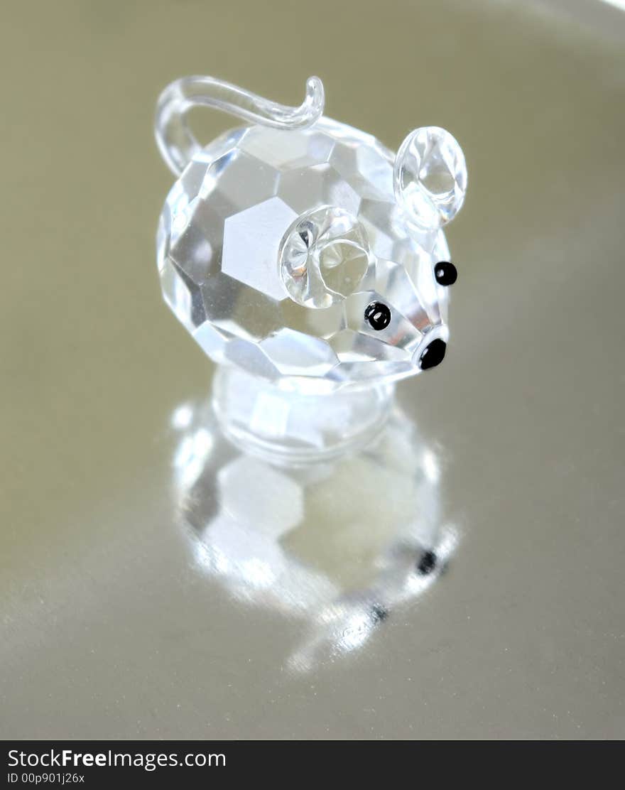 A small souvenir in the form of a glass mousy. Reflection from a metal ridge surface is visible.