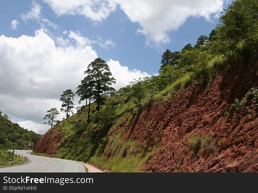 A curved road leads around a large mountain embankment. A curved road leads around a large mountain embankment