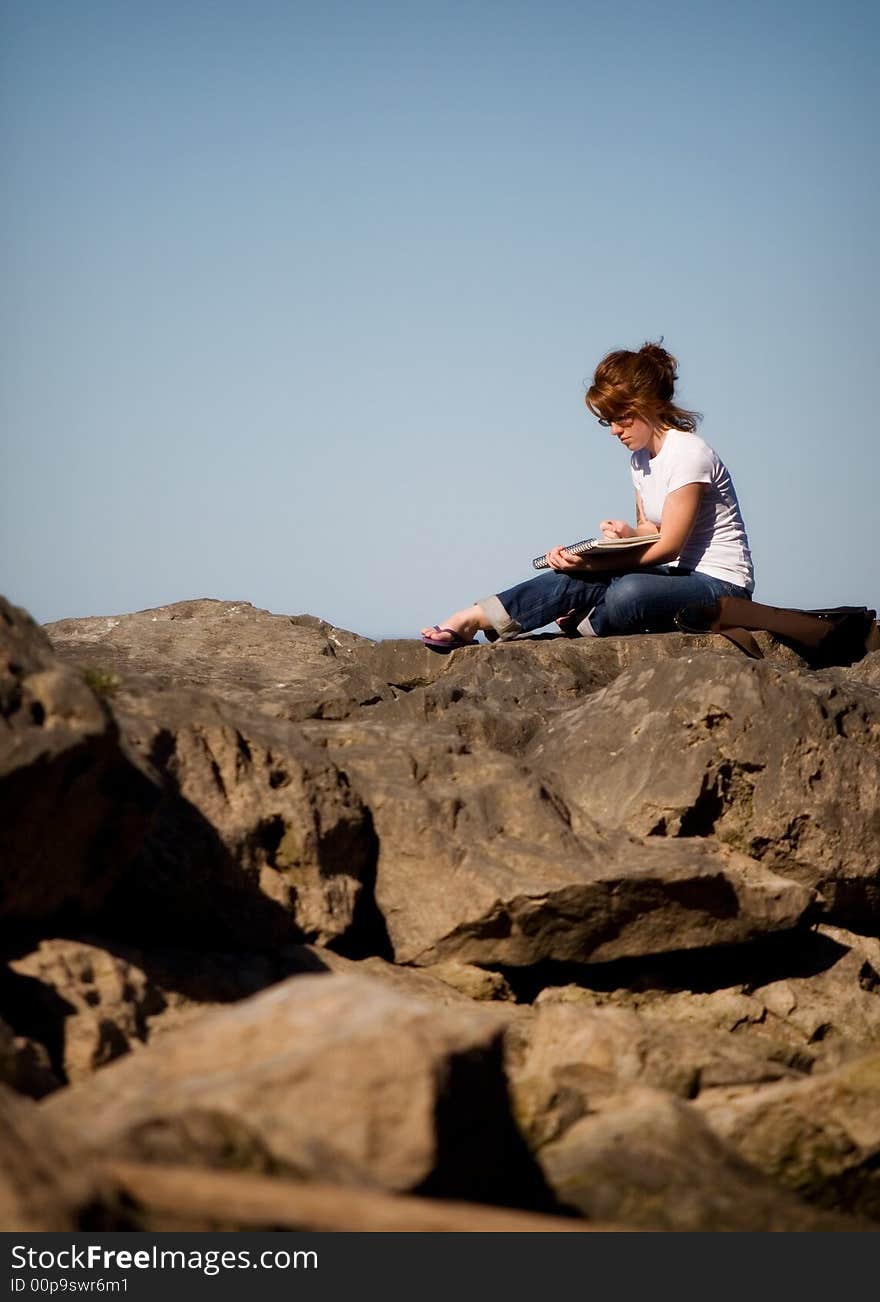 Young woman sketching while sitting high on a pile of boulders. Young woman sketching while sitting high on a pile of boulders.