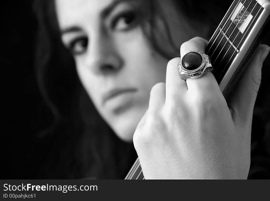 Beautiful brunette on black background playing guitar