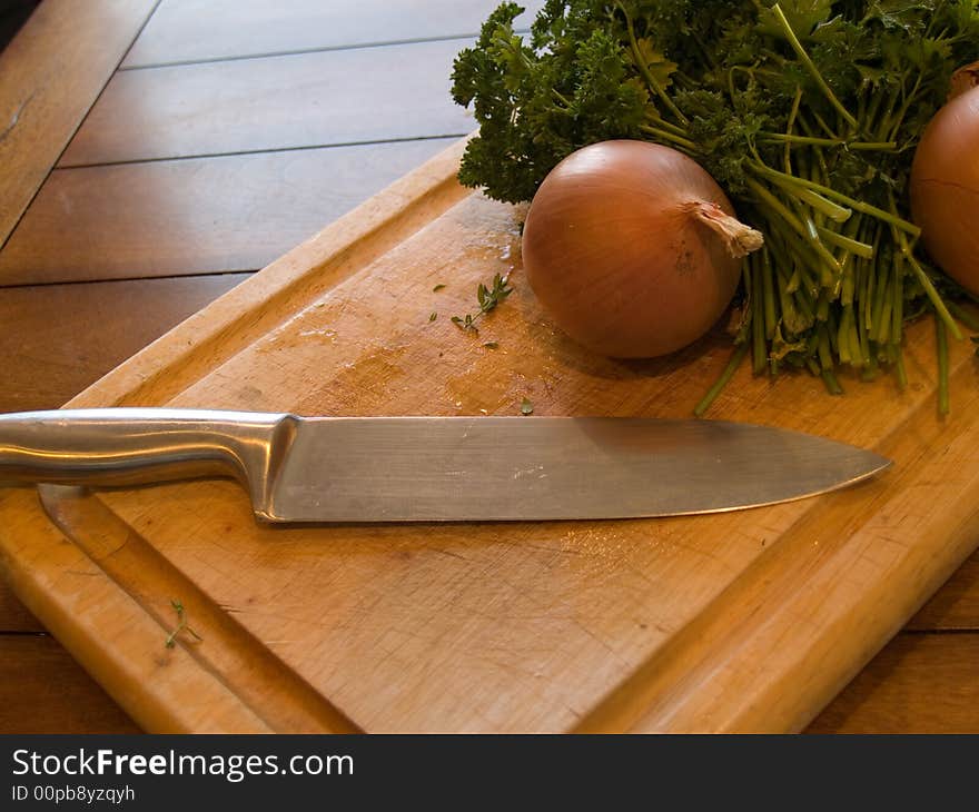 A cutting board with an onion and herbs ready to be cut.