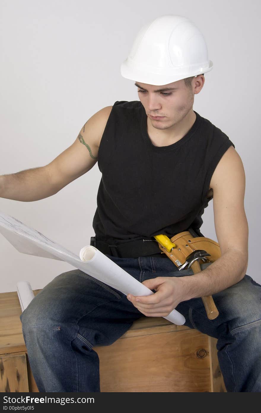 Young man in hard hat and toolbelt studying a set of blueprints. Young man in hard hat and toolbelt studying a set of blueprints.