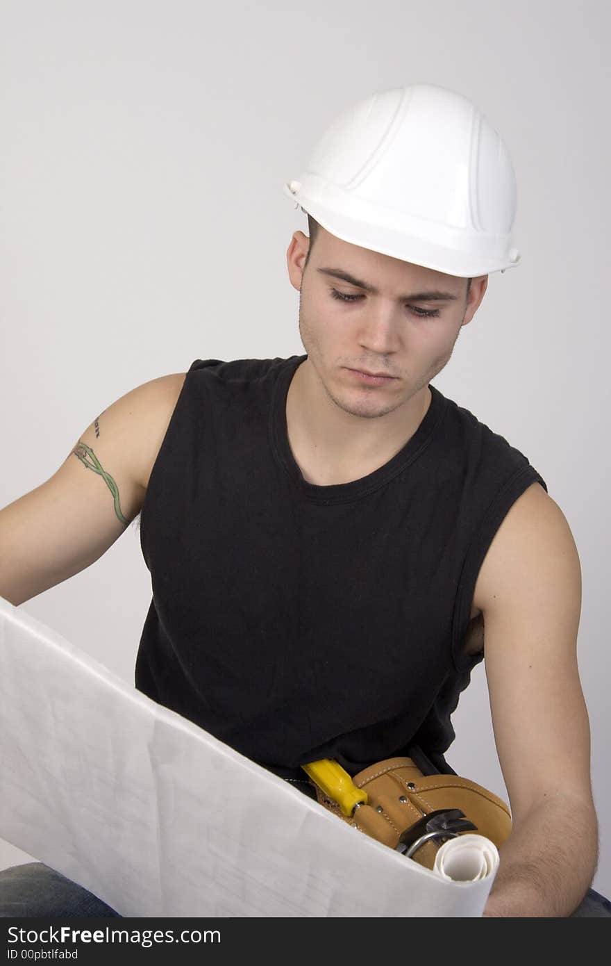 Young man wearing hardhat and toolbelt studying set of blueprints. Young man wearing hardhat and toolbelt studying set of blueprints.