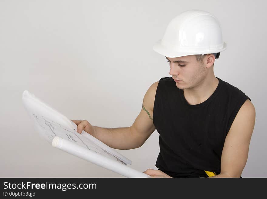 Young man in hardhat looking over a set of blueprints. Young man in hardhat looking over a set of blueprints