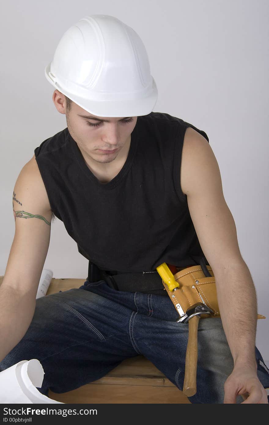 Young man in a hardhat land toolbelt ooking at blueprints. Young man in a hardhat land toolbelt ooking at blueprints