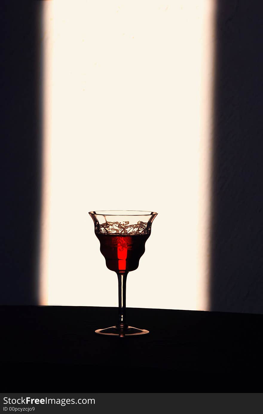 A solitary glass of wine stands beautifully backlit to show the rich color of it’s contents. A solitary glass of wine stands beautifully backlit to show the rich color of it’s contents.