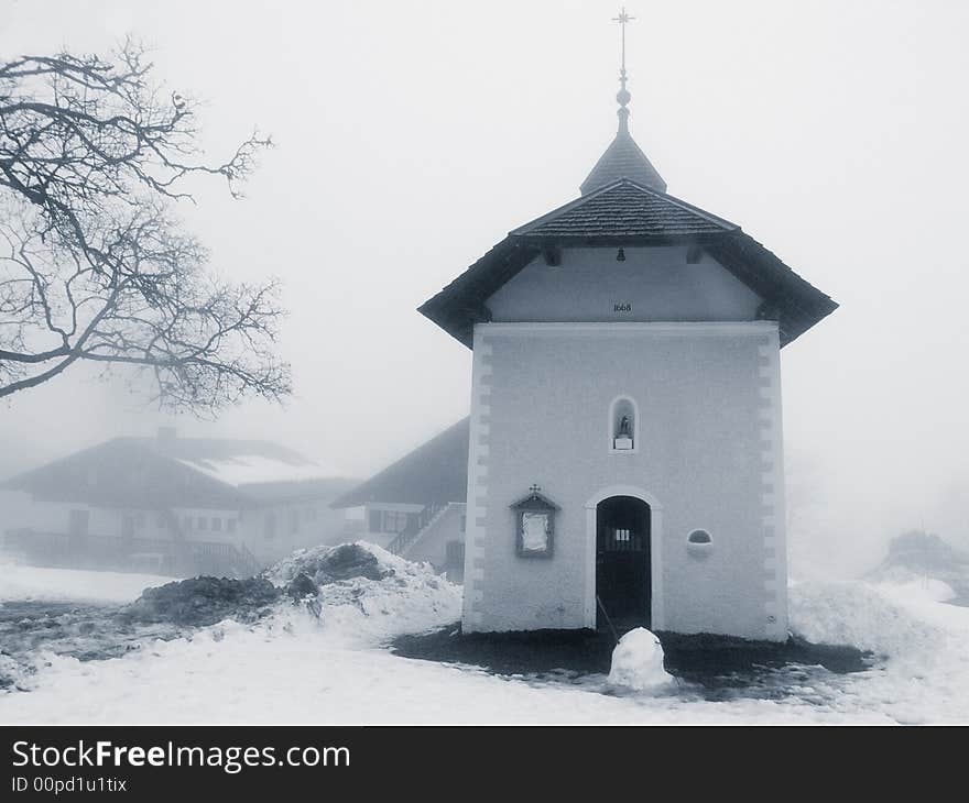 A small church surrounded by snow, with a half-melted snowman in front of the entrance. A small church surrounded by snow, with a half-melted snowman in front of the entrance.