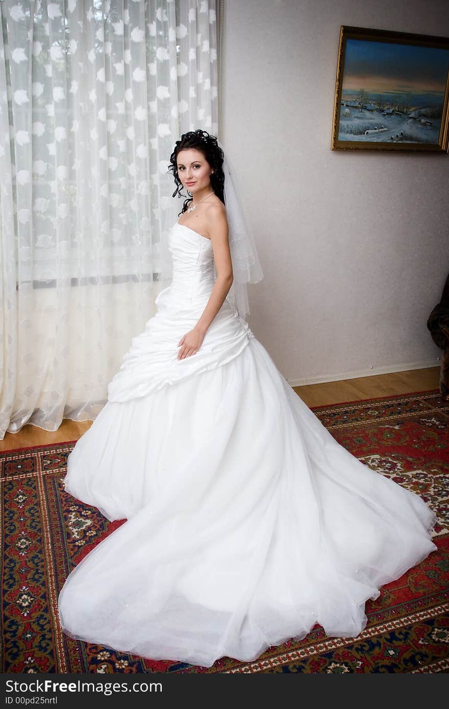 A beatiful bride in a long white dress by the window. A beatiful bride in a long white dress by the window