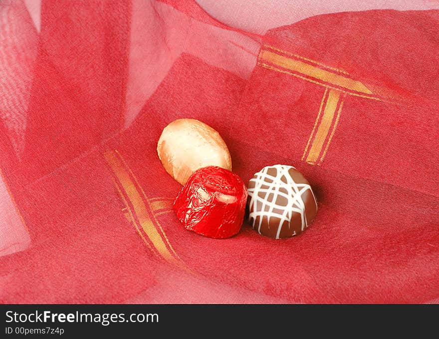 Three fancy chocolates on a piece of red fabric.