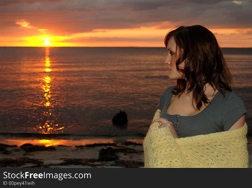 Young woman wrapped in a blanket at the beach looking out to the sunset. Young woman wrapped in a blanket at the beach looking out to the sunset.