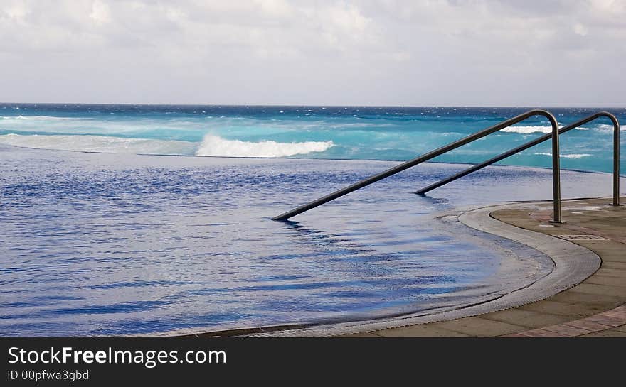 Steps leading into a tranquil blue pool with the ocean in the background. Steps leading into a tranquil blue pool with the ocean in the background