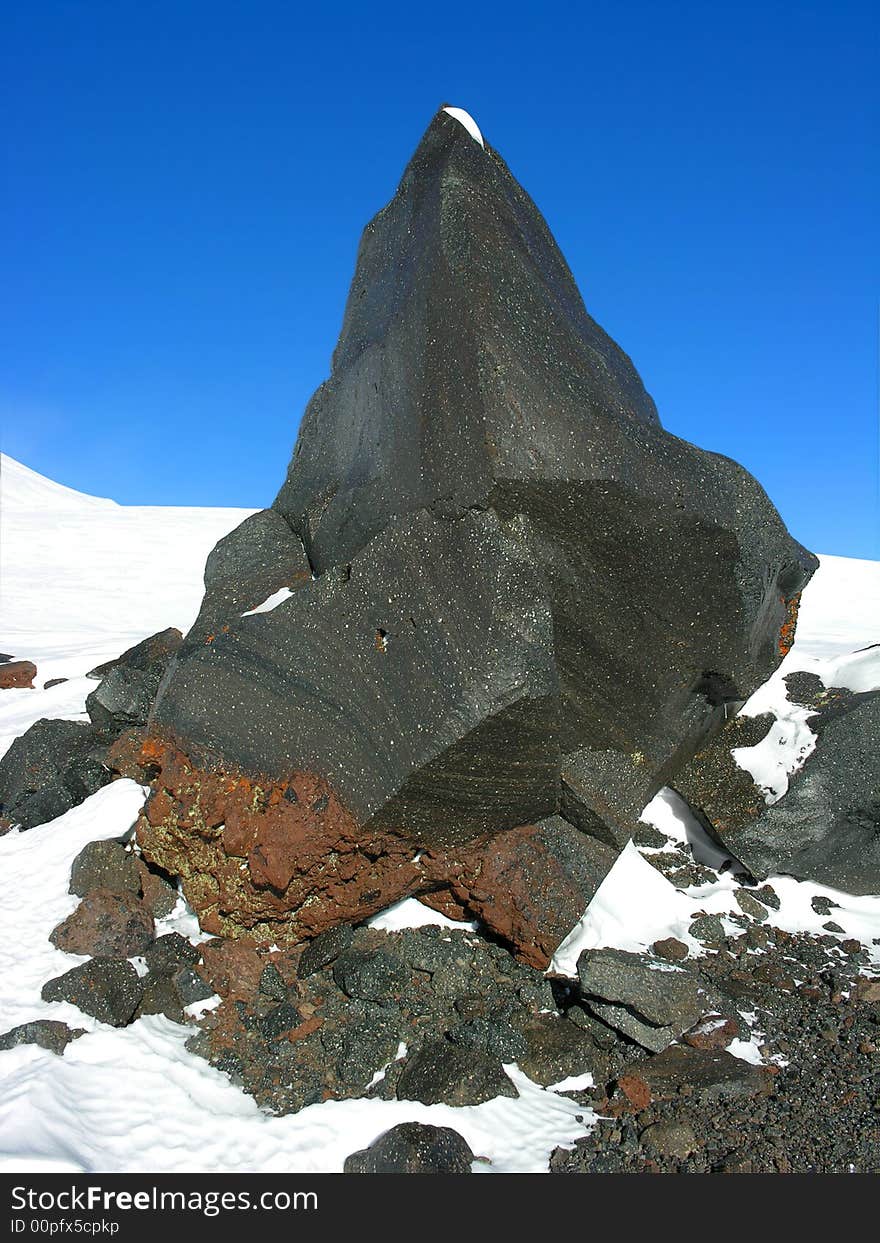 Fragment of a black rock on a snow on a background of the blue sky