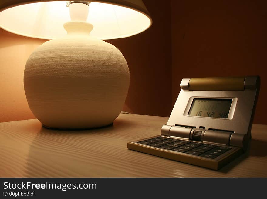 Stone lamp and travel clock on a wooden cabinet in a dark interior of a hotel room. Stone lamp and travel clock on a wooden cabinet in a dark interior of a hotel room