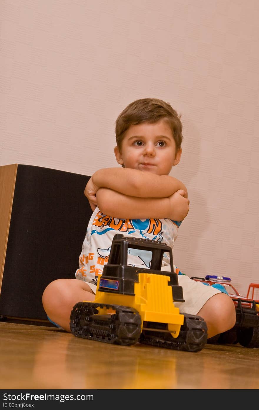 The little boy sitting on a floor with toys.