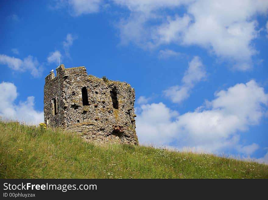 The remains of a medieval tower with green grass in the foreground and a blue sky in the background. The remains of a medieval tower with green grass in the foreground and a blue sky in the background.