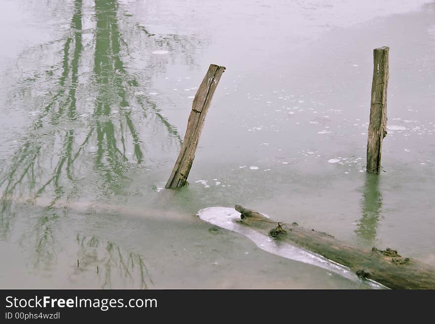 Frozen wooden post in a lake with tree reflection. Frozen wooden post in a lake with tree reflection