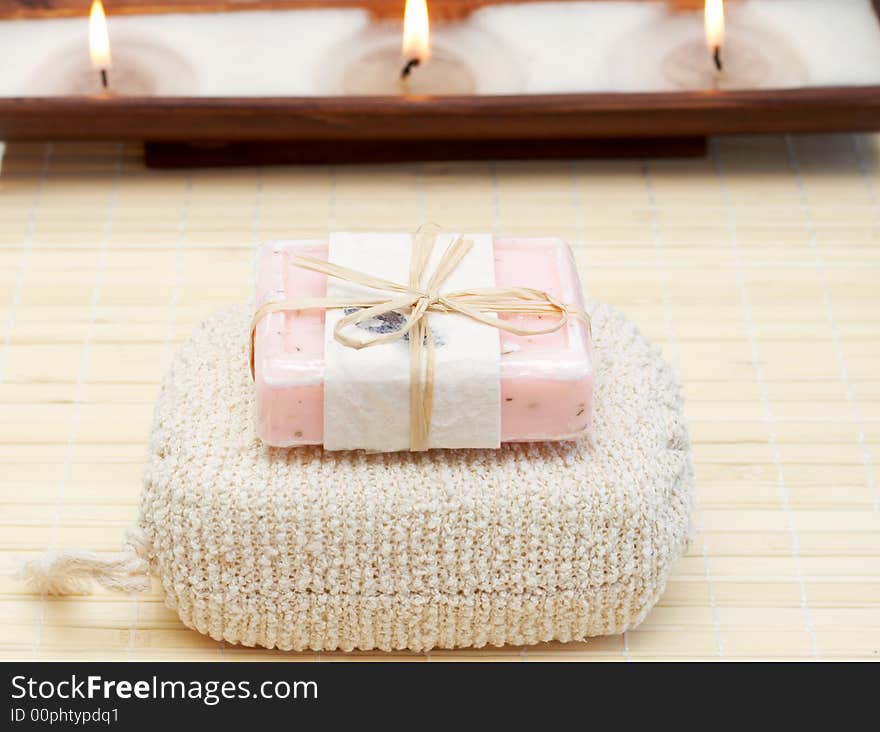 Relaxing spa scene with body products - exfoliating sponge and handmade soap with candles in the background