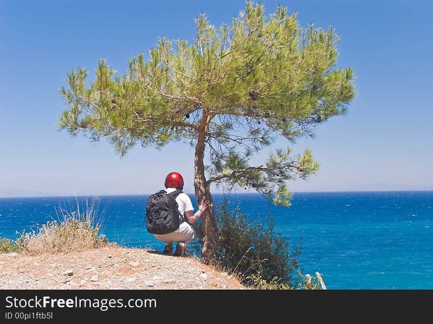 Hiker by a pine-tree on a steep above the sea. Samos island, Greece. Hiker by a pine-tree on a steep above the sea. Samos island, Greece.