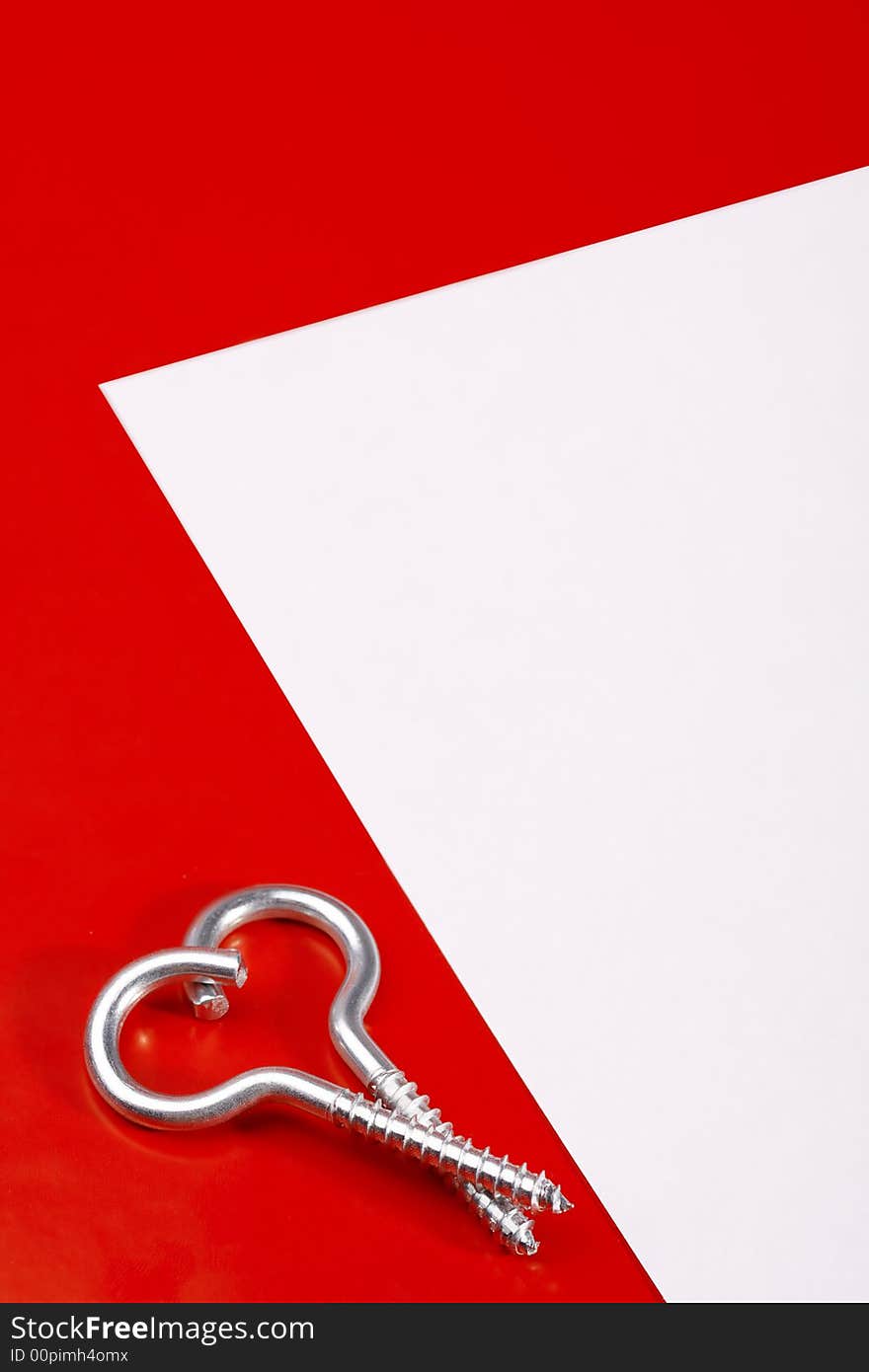 Two spiral bolts laying in the form of heart on a red background near to a leaf of a paper. Two spiral bolts laying in the form of heart on a red background near to a leaf of a paper