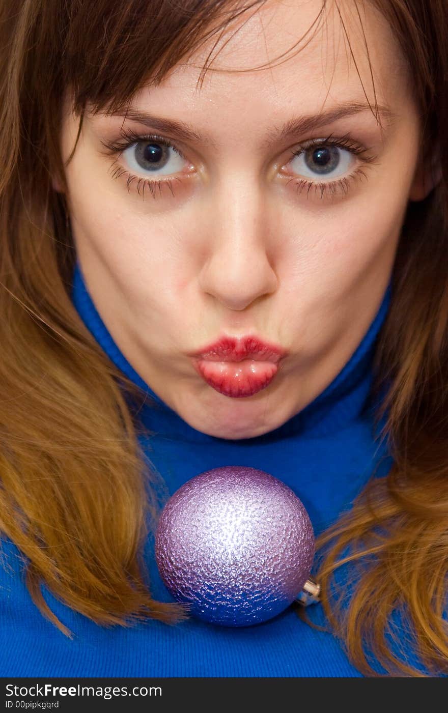 A girl, placing her lips into kiss, with christmas ball on her chest. A girl, placing her lips into kiss, with christmas ball on her chest