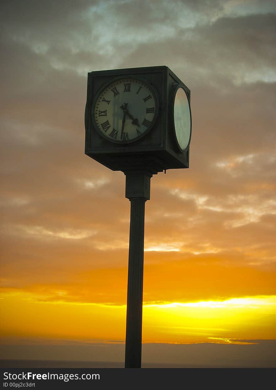 A clock in the foreground and sunset in the background