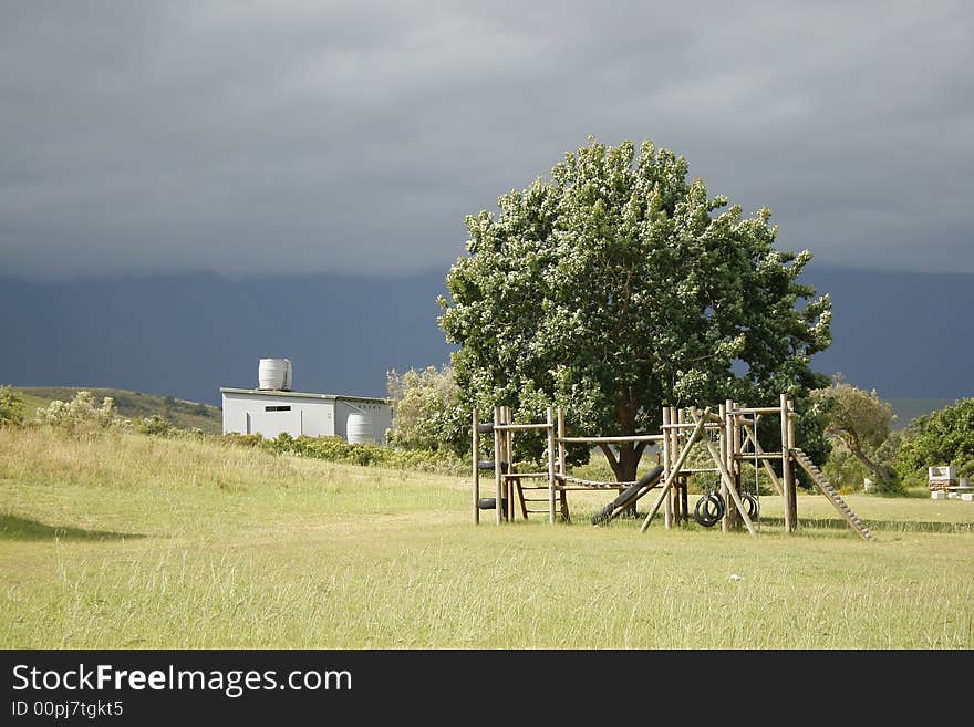 A child's play ground with a climber, a tree and a bathroom in the background. A child's play ground with a climber, a tree and a bathroom in the background