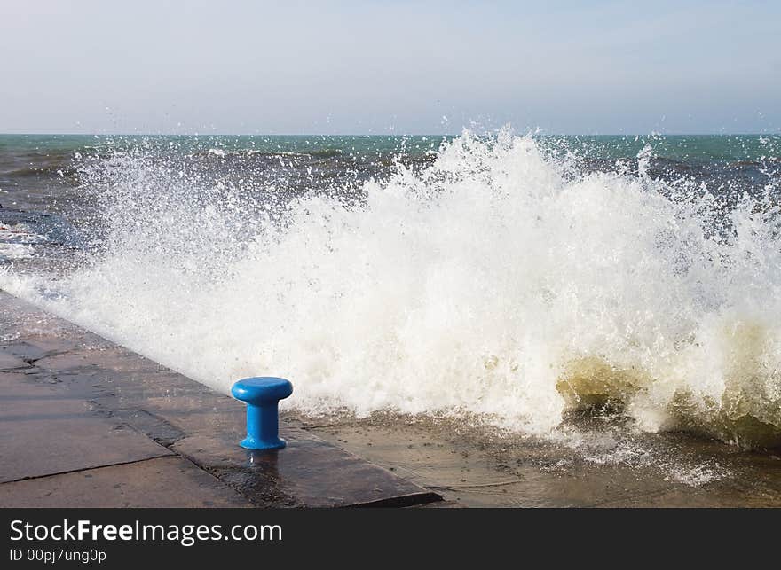 Lake Michigan wave crashing into the pier, with blue mooring bollard, at the channel mouth in Grand Haven. Lake Michigan wave crashing into the pier, with blue mooring bollard, at the channel mouth in Grand Haven