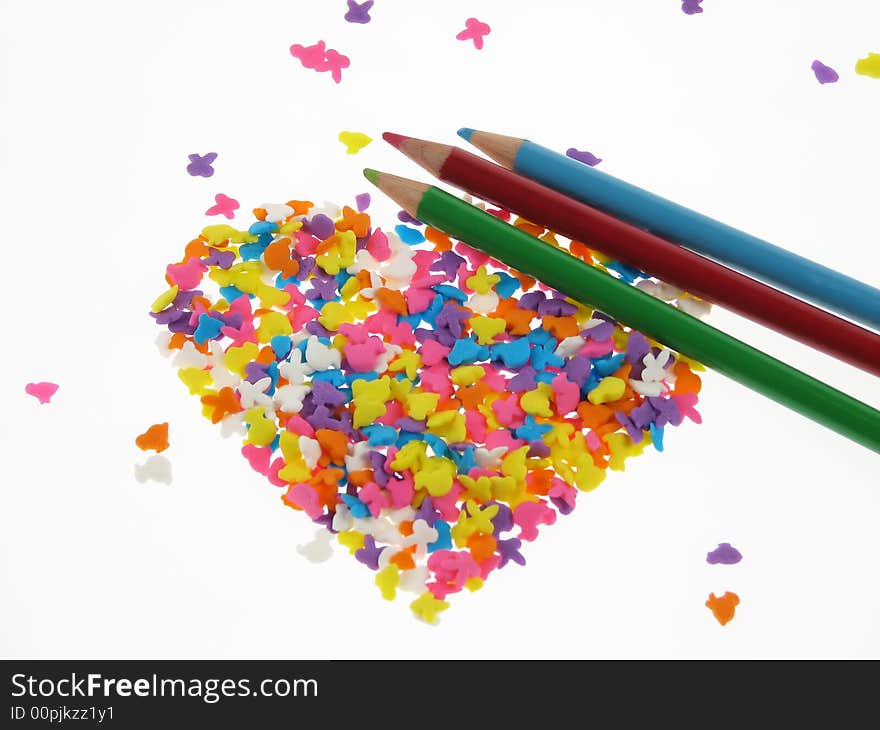 Crayons together with colorful candies shaped in heart form placed on white background. Crayons together with colorful candies shaped in heart form placed on white background