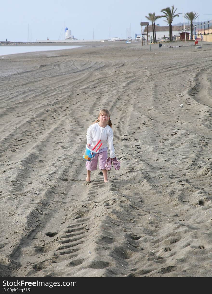 A young girl walking along the beach looking fed up carrying her bucket and spade. A young girl walking along the beach looking fed up carrying her bucket and spade