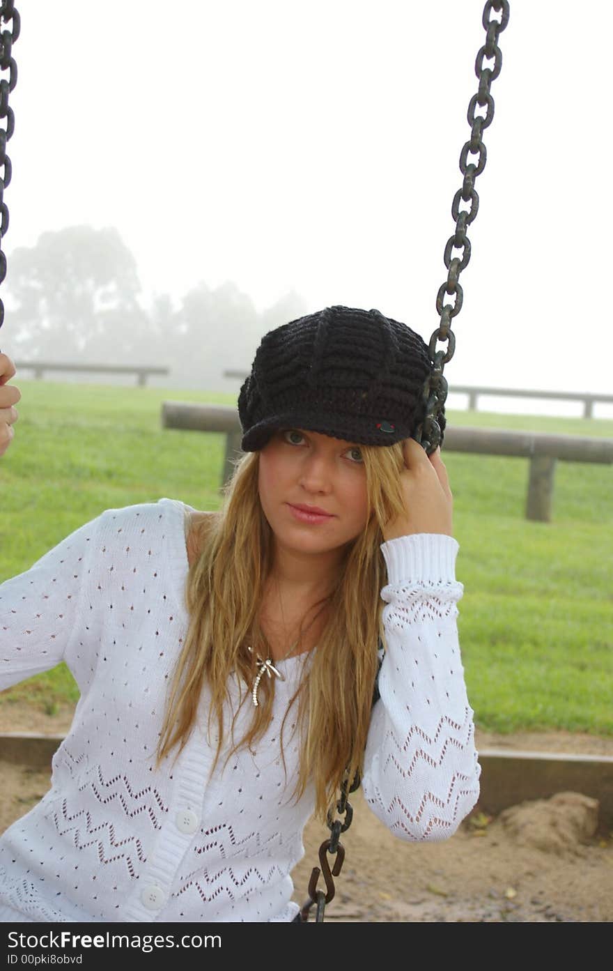 Girl sitting on a swing in the fog over a grassy hill. Girl sitting on a swing in the fog over a grassy hill