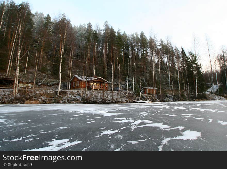 Wooden cottage in the forest and lake in winter