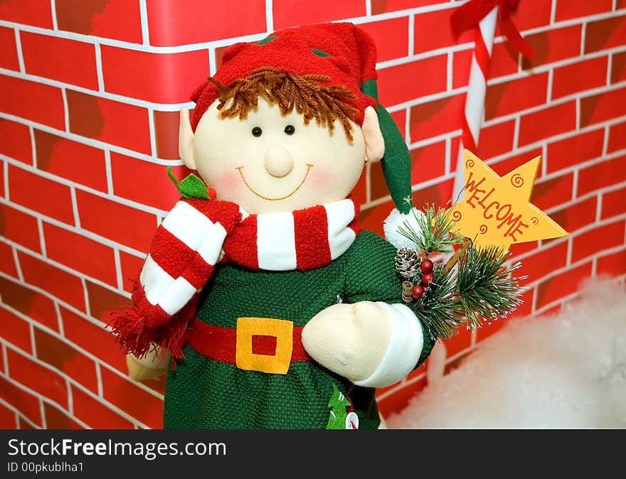 A colorfully stuffed toy snowman holding a welcome sign, all dressed up in winter clothing against a red brick background. A colorfully stuffed toy snowman holding a welcome sign, all dressed up in winter clothing against a red brick background.