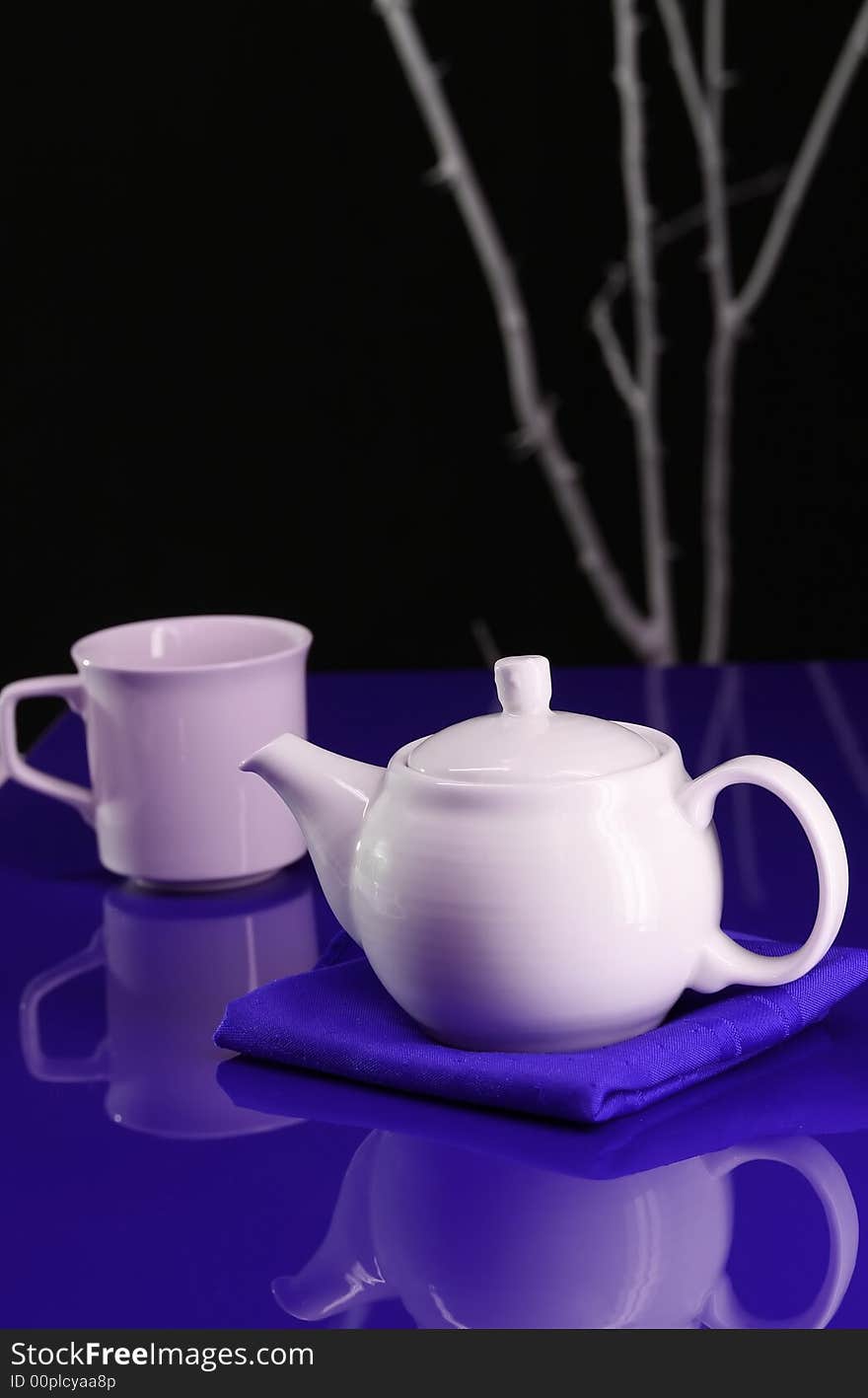 A modern table setting with a teapot and cup on a blue background. A modern table setting with a teapot and cup on a blue background