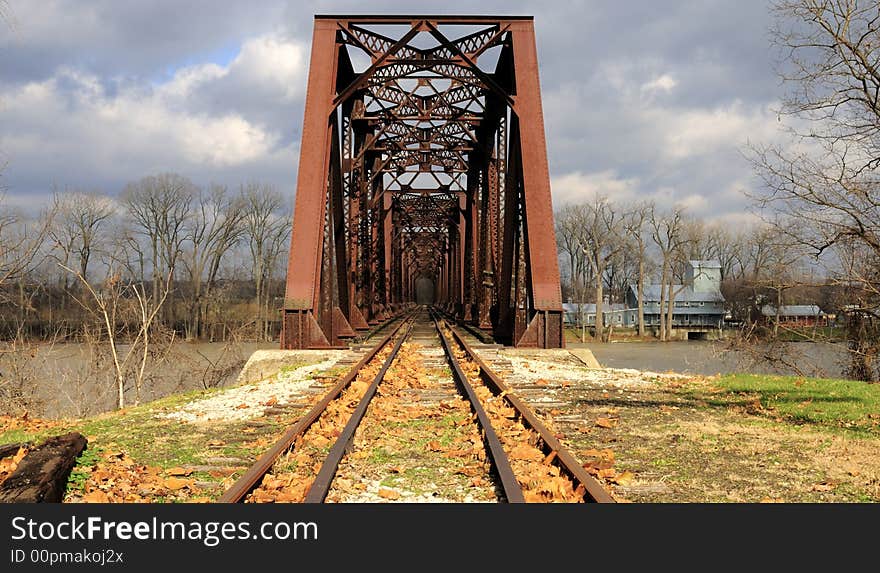 This classic steel railroad bridge is of riveted truss construction. The bridge truss with deck plate girders provide an approach to the structure, which sits on concrete piers. There is lattice present on the bracing and cowling. This classic steel railroad bridge is of riveted truss construction. The bridge truss with deck plate girders provide an approach to the structure, which sits on concrete piers. There is lattice present on the bracing and cowling.