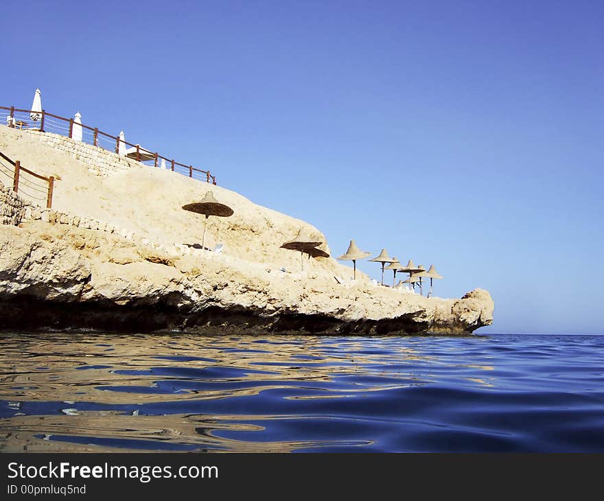 Small rocky beach with sun shades viewed from the sea. Small rocky beach with sun shades viewed from the sea