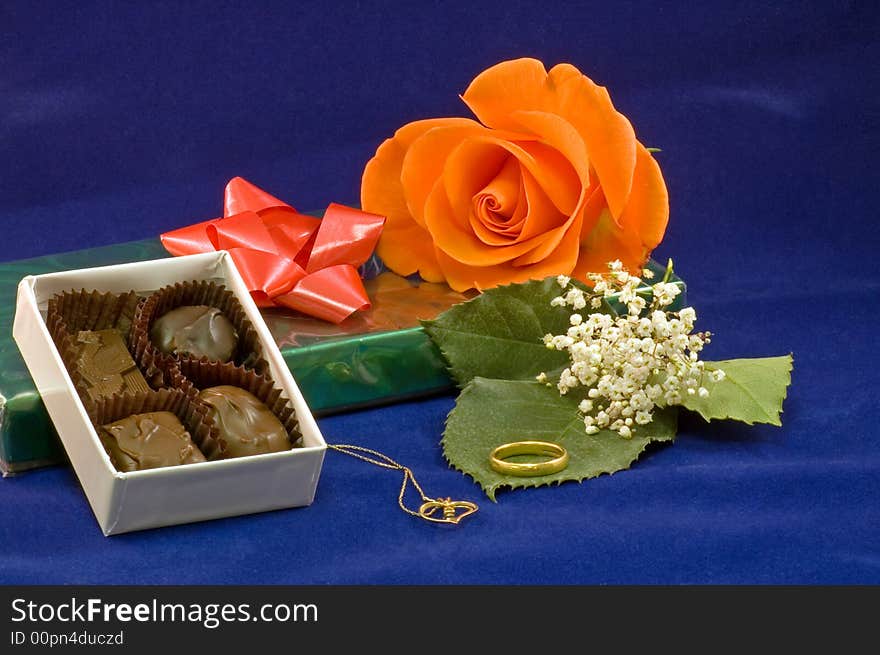 A closeup view of a chocolates on a box with a peach colored rose and gold necklace and baby's breath. A closeup view of a chocolates on a box with a peach colored rose and gold necklace and baby's breath.