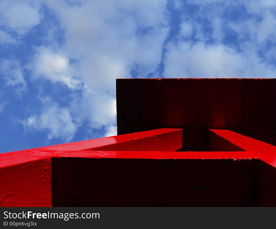 Red water tower in sunlight contrasting with bright blue sky and scattered clouds