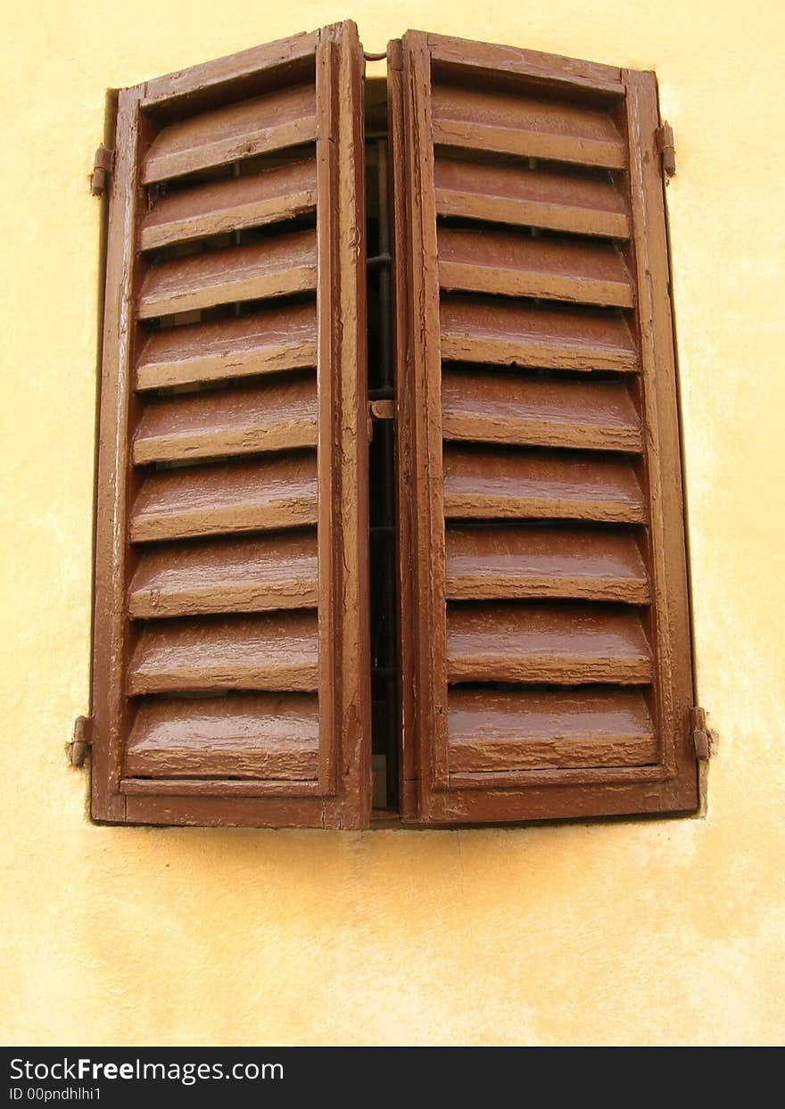 Two brown closed window shutters on a beige wall of a house in Italy