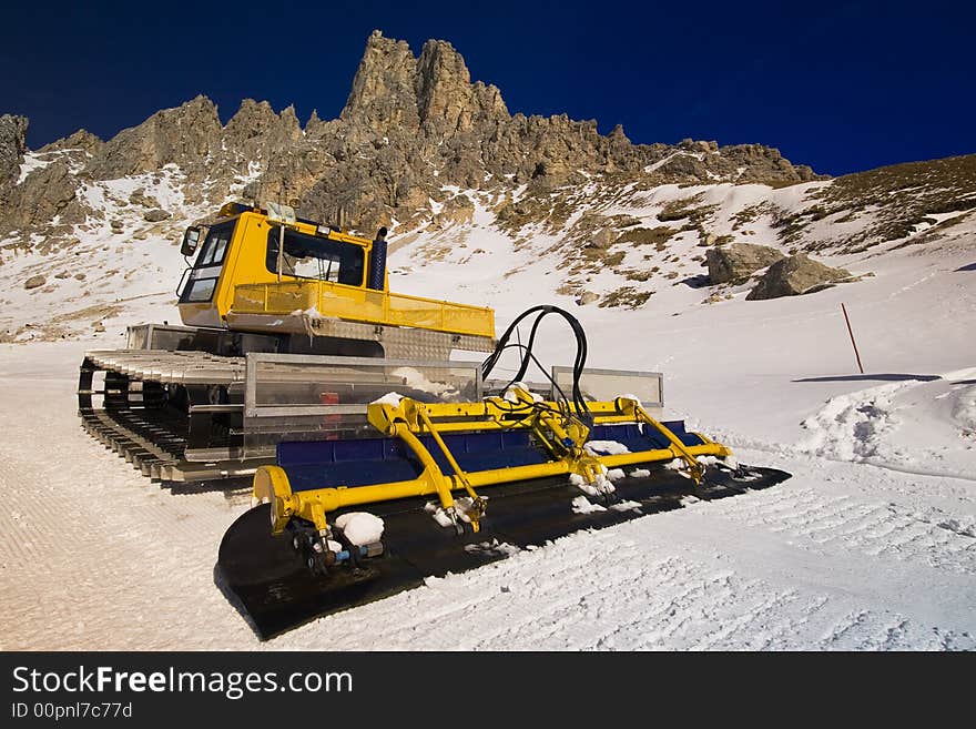 A snow plough on a mountain ski slope with jagged peaks in the background. A snow plough on a mountain ski slope with jagged peaks in the background.