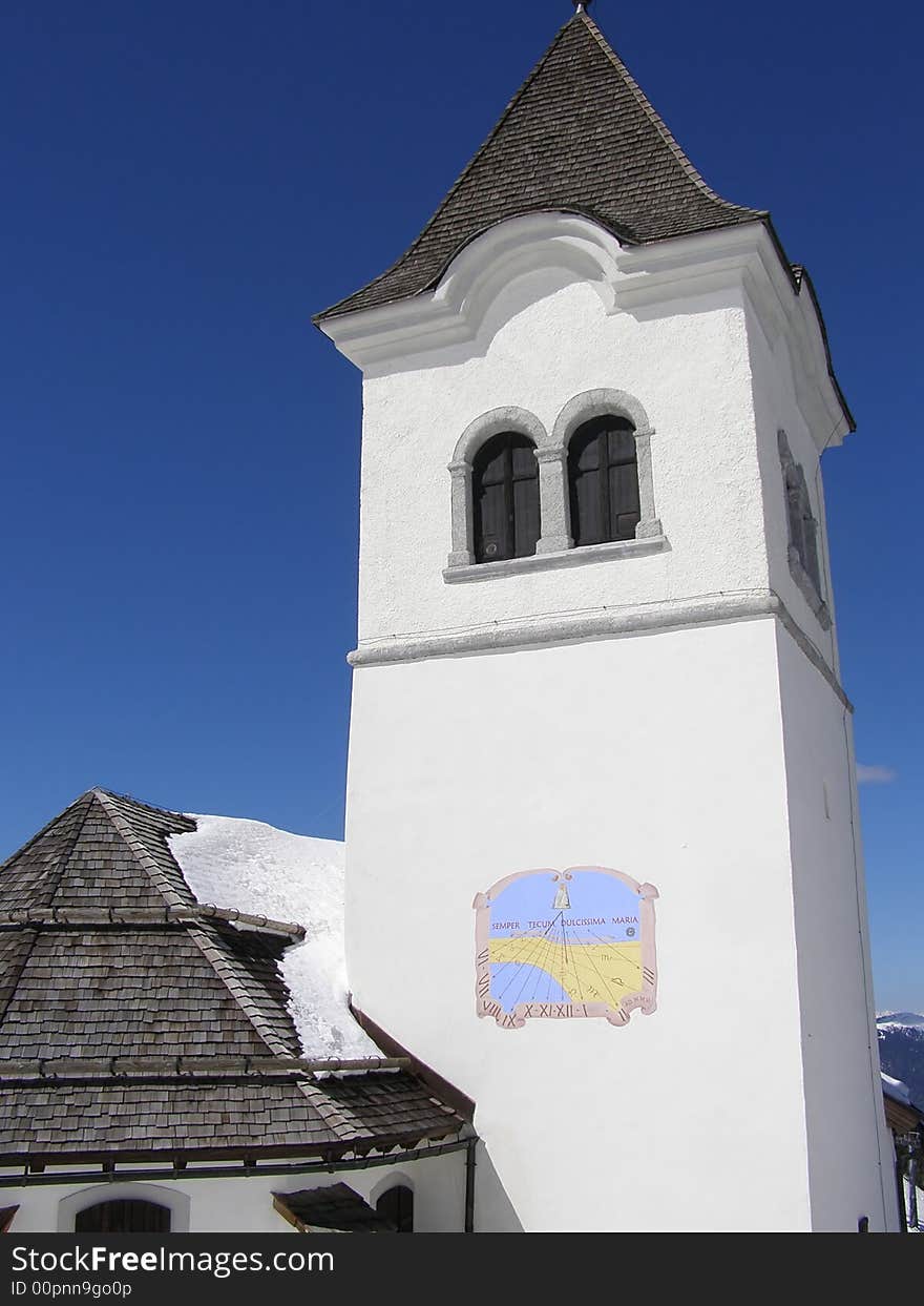 Church tower and apside exterior in the mountains, sunny winter day, snow on church roof, tower with sun clock, clear blue sky background. Church tower and apside exterior in the mountains, sunny winter day, snow on church roof, tower with sun clock, clear blue sky background